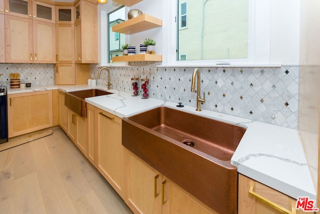 kitchen with decorative backsplash, light brown cabinets, light wood-type flooring, light stone counters, and sink