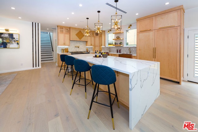 kitchen featuring light stone countertops, light brown cabinets, a spacious island, and light hardwood / wood-style floors