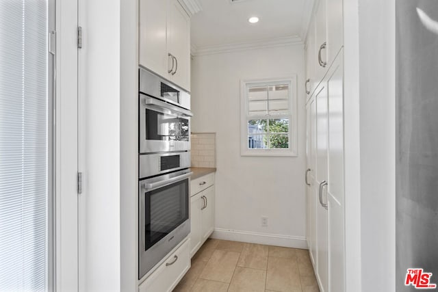 kitchen with stainless steel double oven, white cabinetry, decorative backsplash, ornamental molding, and light tile patterned floors