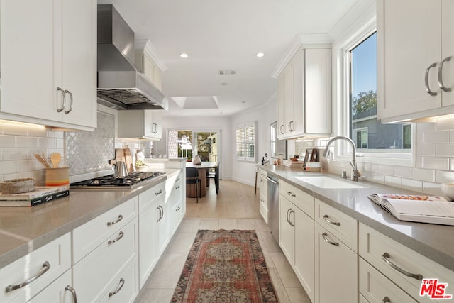 kitchen featuring tasteful backsplash, light tile patterned flooring, wall chimney exhaust hood, white cabinets, and sink