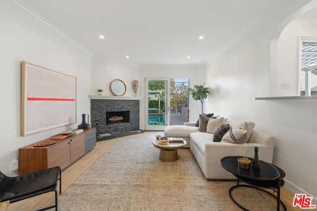 living room with light hardwood / wood-style floors, ornamental molding, and a stone fireplace