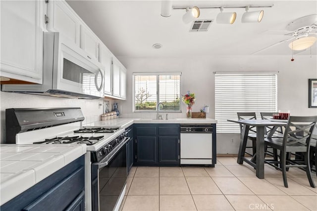 kitchen featuring white cabinets, tile countertops, light tile patterned floors, and white appliances