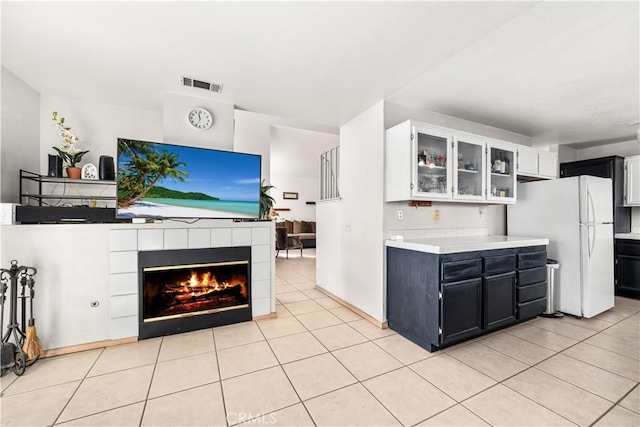 kitchen with white cabinets, a tiled fireplace, light tile patterned floors, and white refrigerator