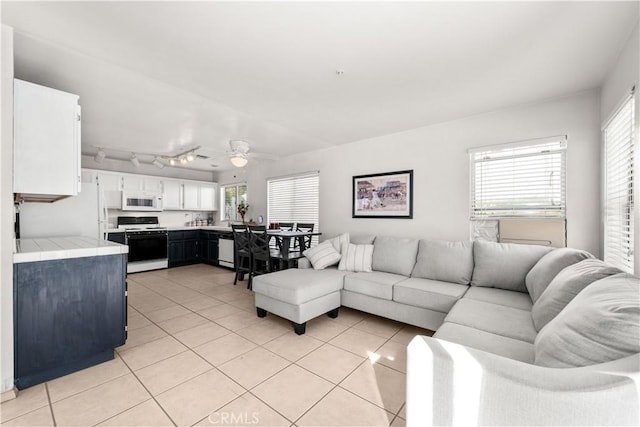 tiled living room with ceiling fan, track lighting, and a healthy amount of sunlight