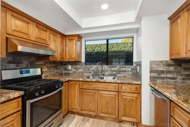 kitchen with a sink, stainless steel appliances, range hood, and brown cabinetry