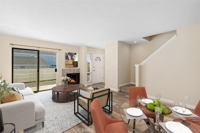 living room featuring stairway, baseboards, a lit fireplace, and wood finished floors