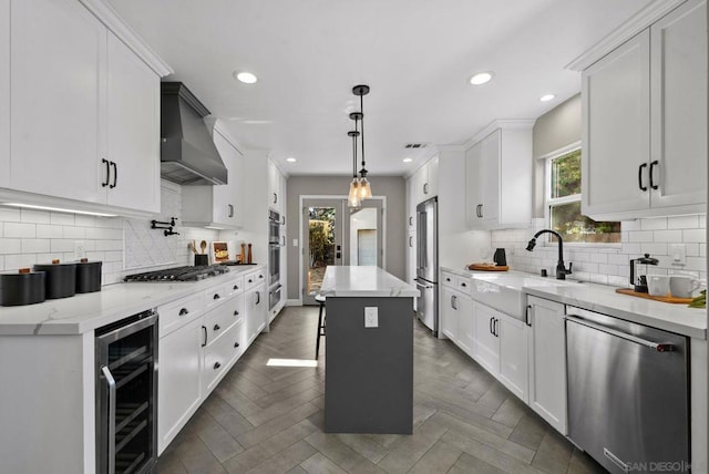 kitchen with white cabinets, appliances with stainless steel finishes, wall chimney exhaust hood, a kitchen island, and wine cooler