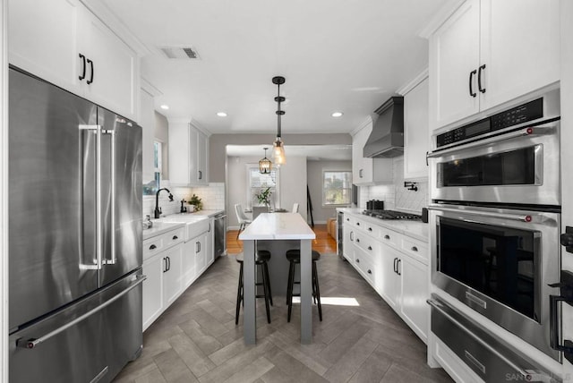 kitchen with white cabinets, appliances with stainless steel finishes, premium range hood, and pendant lighting