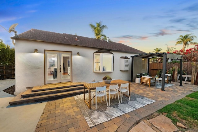 back house at dusk with french doors, a pergola, a patio area, and an outdoor living space