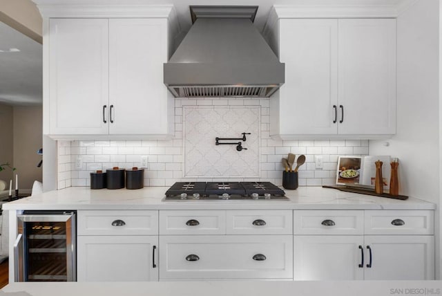 kitchen with custom exhaust hood, beverage cooler, white cabinets, and backsplash