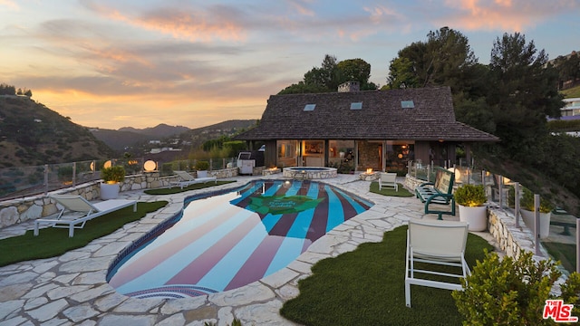 pool at dusk with a mountain view, a patio, and an in ground hot tub