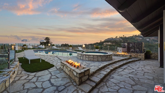 patio terrace at dusk featuring a swimming pool with hot tub and a fire pit