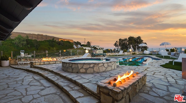 pool at dusk with an outdoor fire pit, an in ground hot tub, and a patio