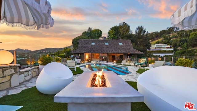 pool at dusk with a patio area, an outbuilding, a mountain view, and a fire pit