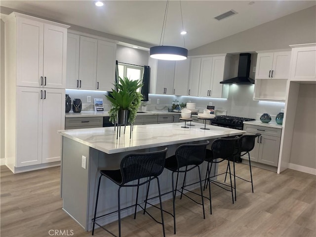 kitchen with decorative light fixtures, wall chimney range hood, a center island, white cabinetry, and light stone countertops