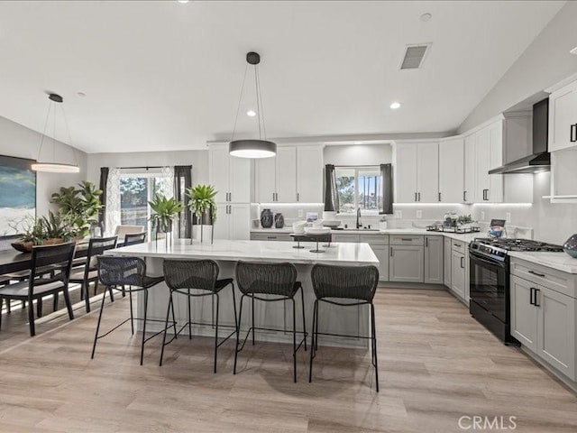 kitchen featuring gas stove, a center island with sink, sink, hanging light fixtures, and a kitchen breakfast bar