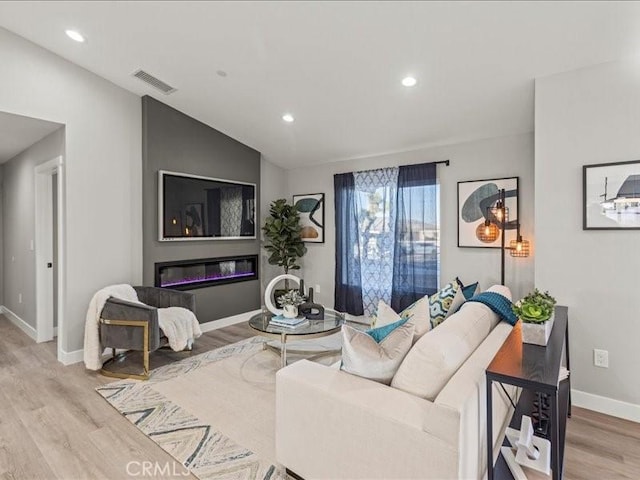 living room featuring a large fireplace, light wood-type flooring, and vaulted ceiling