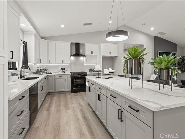 kitchen with vaulted ceiling, wall chimney range hood, a center island, white cabinets, and gas range