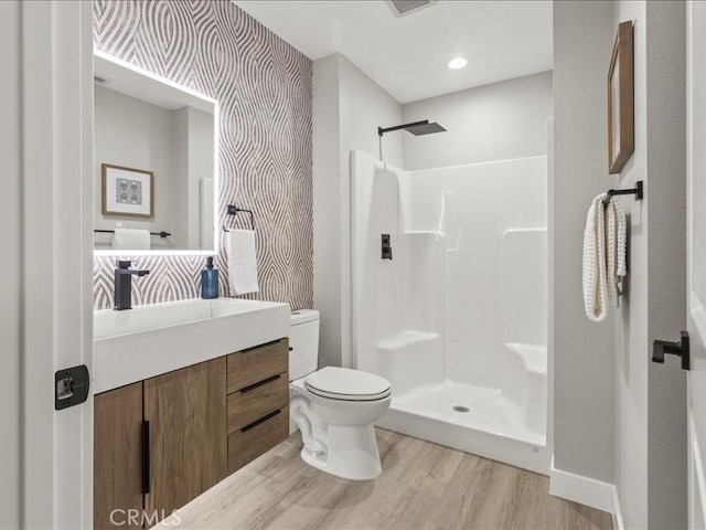 bathroom with hardwood / wood-style flooring, toilet, walk in shower, and vanity