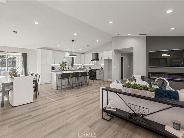 living room featuring lofted ceiling, sink, and light hardwood / wood-style floors