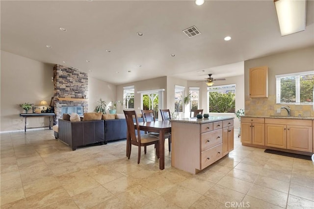 kitchen with ceiling fan, a fireplace, a center island, sink, and light brown cabinetry