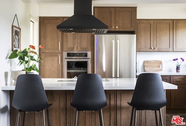 kitchen with a breakfast bar area, stainless steel appliances, and wall chimney exhaust hood