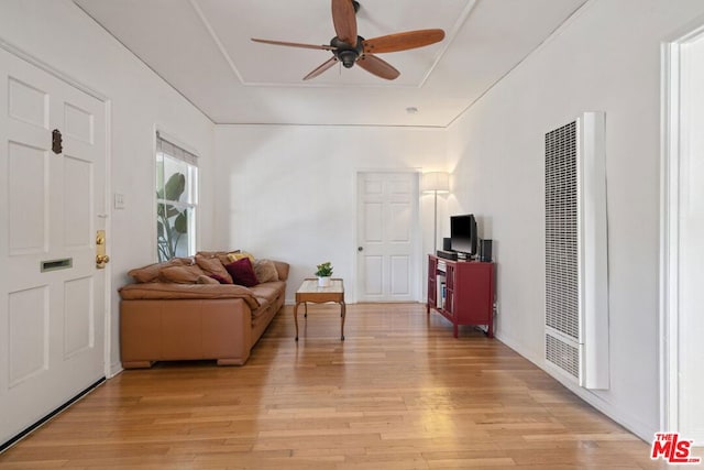 living room with ceiling fan, a tray ceiling, and light hardwood / wood-style flooring