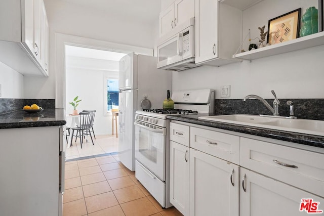 kitchen with sink, white appliances, white cabinetry, light tile patterned floors, and dark stone counters