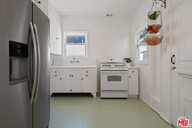 kitchen with white cabinets, stainless steel fridge, sink, and white range oven