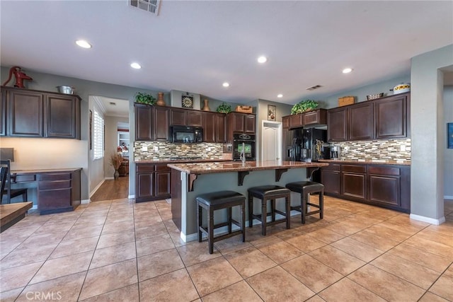 kitchen featuring black appliances, dark brown cabinetry, a kitchen breakfast bar, an island with sink, and light tile patterned floors