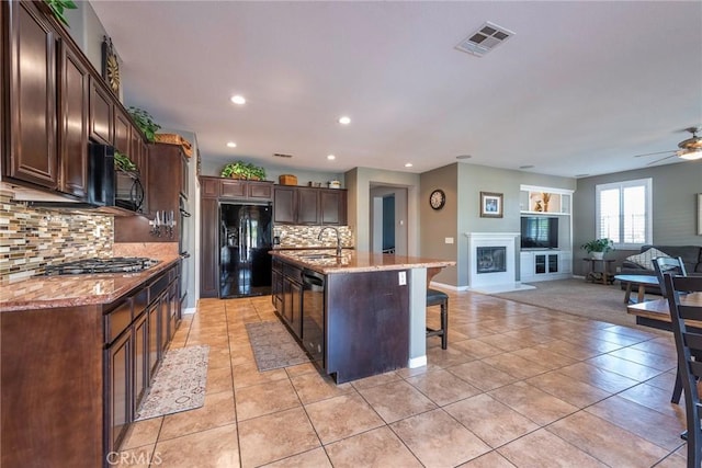 kitchen featuring tasteful backsplash, a center island with sink, black appliances, sink, and light tile patterned floors