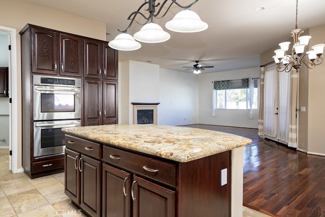 kitchen featuring light stone counters, hanging light fixtures, dark brown cabinets, stainless steel double oven, and a fireplace