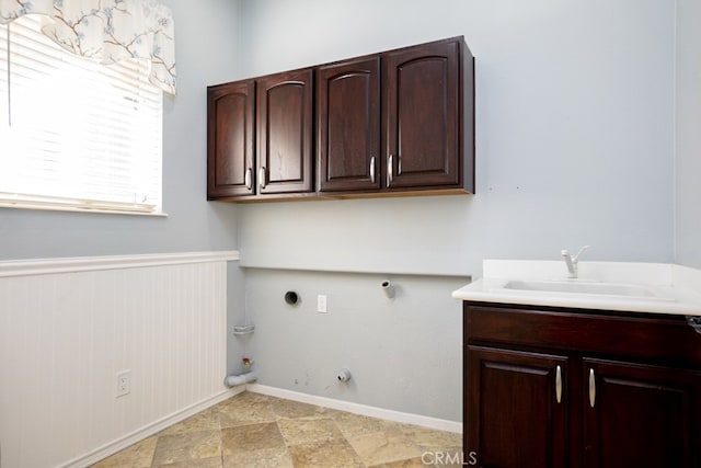 laundry area featuring cabinet space, baseboards, wainscoting, gas dryer hookup, and a sink