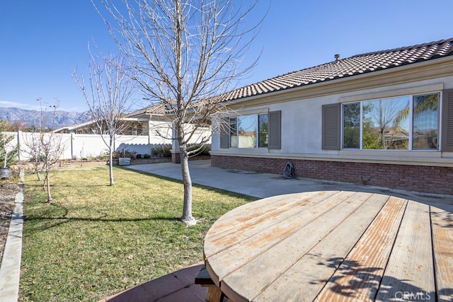 exterior space with a lawn, stucco siding, a tiled roof, fence, and brick siding