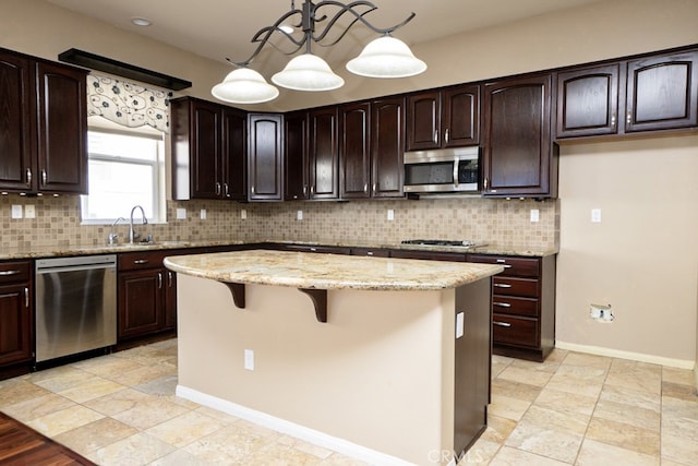 kitchen featuring a kitchen island, backsplash, light stone countertops, stainless steel appliances, and a sink