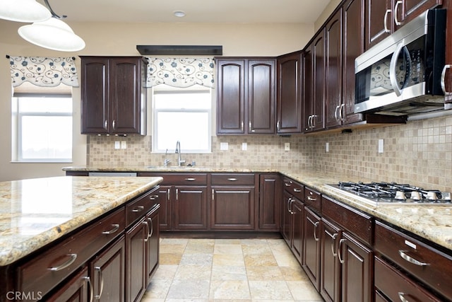 kitchen featuring dark brown cabinetry, a sink, appliances with stainless steel finishes, decorative backsplash, and light stone countertops