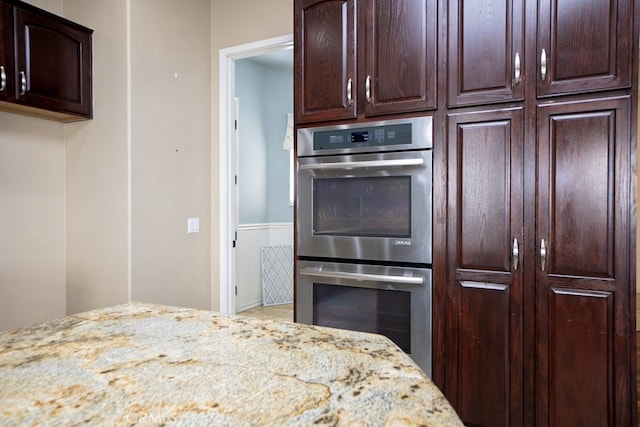 kitchen with light stone counters, stainless steel double oven, and dark brown cabinetry