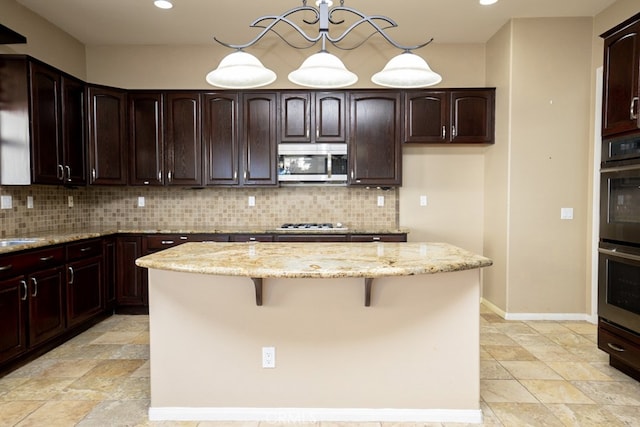 kitchen with light stone counters, stainless steel appliances, hanging light fixtures, a center island, and tasteful backsplash