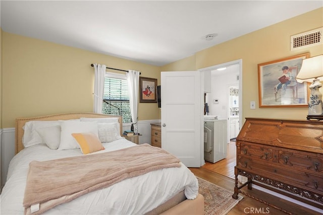 bedroom featuring connected bathroom, washer / dryer, and light wood-type flooring