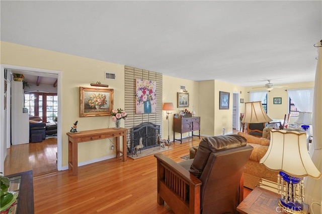 living room with a brick fireplace, light hardwood / wood-style flooring, and ceiling fan