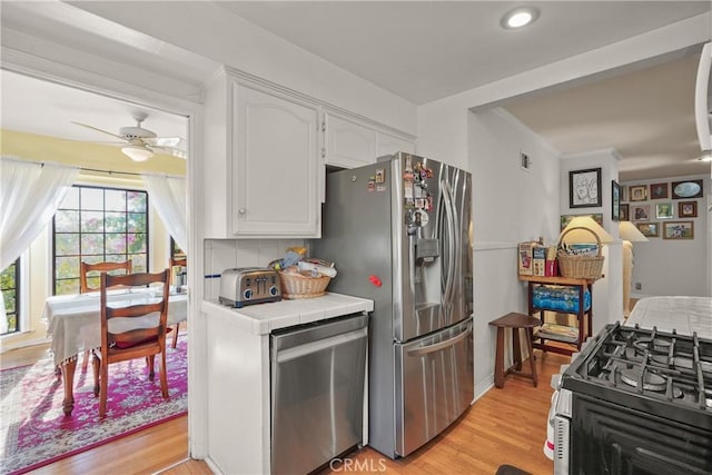 kitchen featuring tile counters, appliances with stainless steel finishes, white cabinets, light wood-type flooring, and ceiling fan