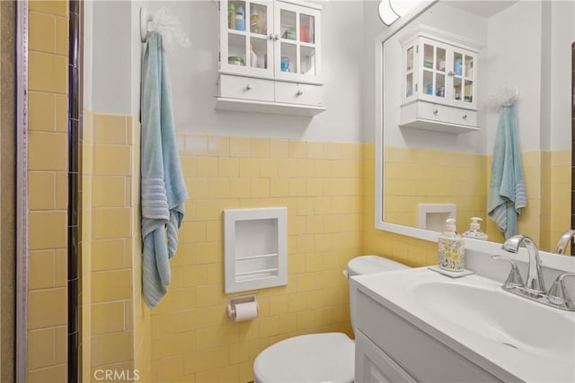 bathroom featuring toilet, vanity, and tile walls