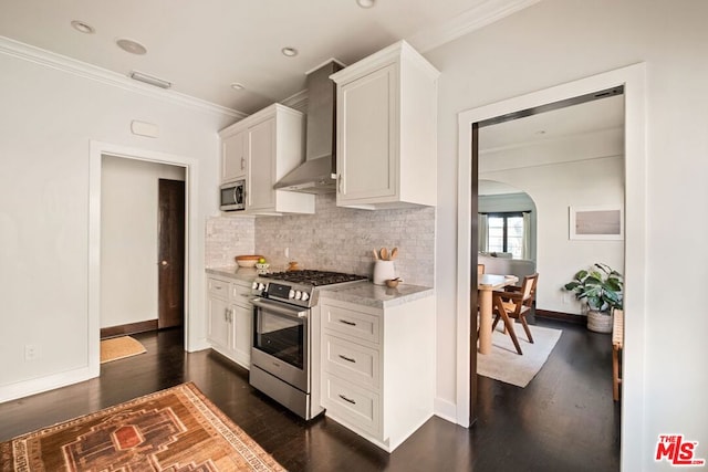 kitchen featuring white cabinets, appliances with stainless steel finishes, wall chimney range hood, dark hardwood / wood-style flooring, and crown molding