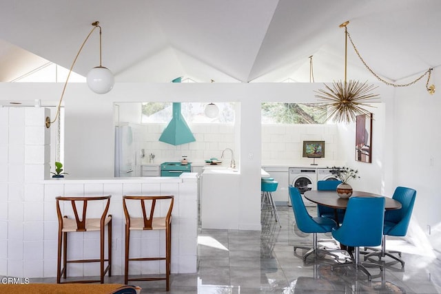 interior space with vaulted ceiling, kitchen peninsula, sink, washer and clothes dryer, and white refrigerator