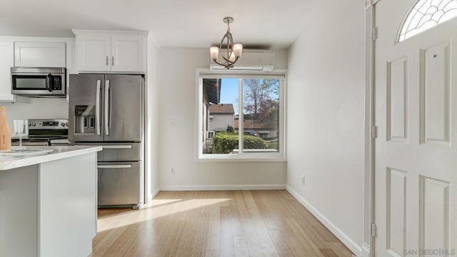 kitchen with white cabinetry, stainless steel appliances, decorative light fixtures, a notable chandelier, and light hardwood / wood-style flooring