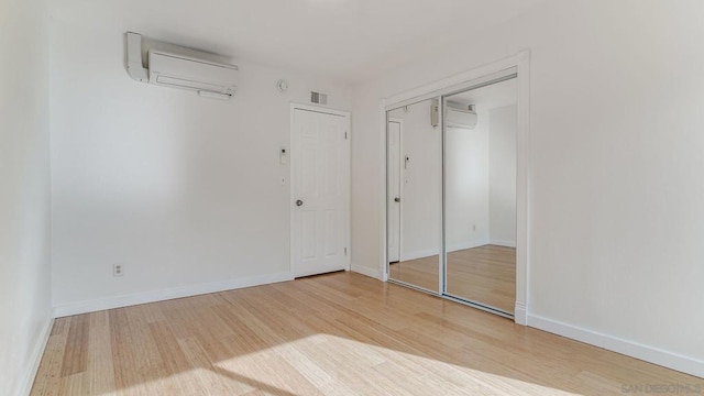 unfurnished bedroom with a wall mounted AC, a closet, and hardwood / wood-style floors