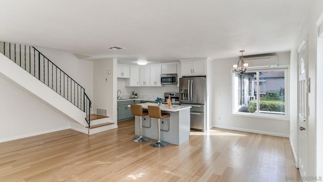 kitchen featuring light hardwood / wood-style floors, an island with sink, appliances with stainless steel finishes, decorative light fixtures, and a kitchen breakfast bar