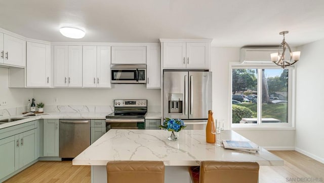 kitchen featuring decorative light fixtures, light hardwood / wood-style floors, a center island, white cabinetry, and appliances with stainless steel finishes