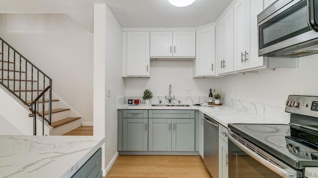 kitchen featuring stainless steel appliances, white cabinetry, light stone counters, and sink