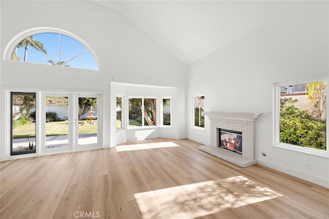 unfurnished living room featuring a brick fireplace, light hardwood / wood-style flooring, and high vaulted ceiling